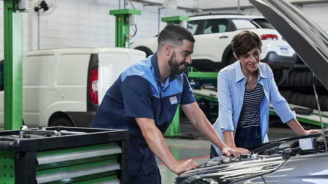 Mecânico da Axial Car explicando um reparo a uma cliente, com o capô aberto na oficina